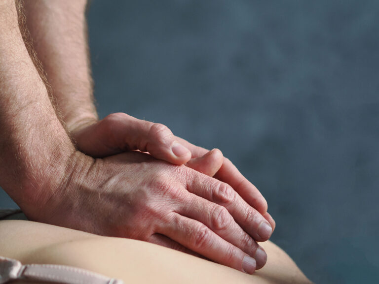 Dłonie fizjoterapeuty na plecach pacjentki podczas rehabilitacji kręgosłupa w przychodni Biomed